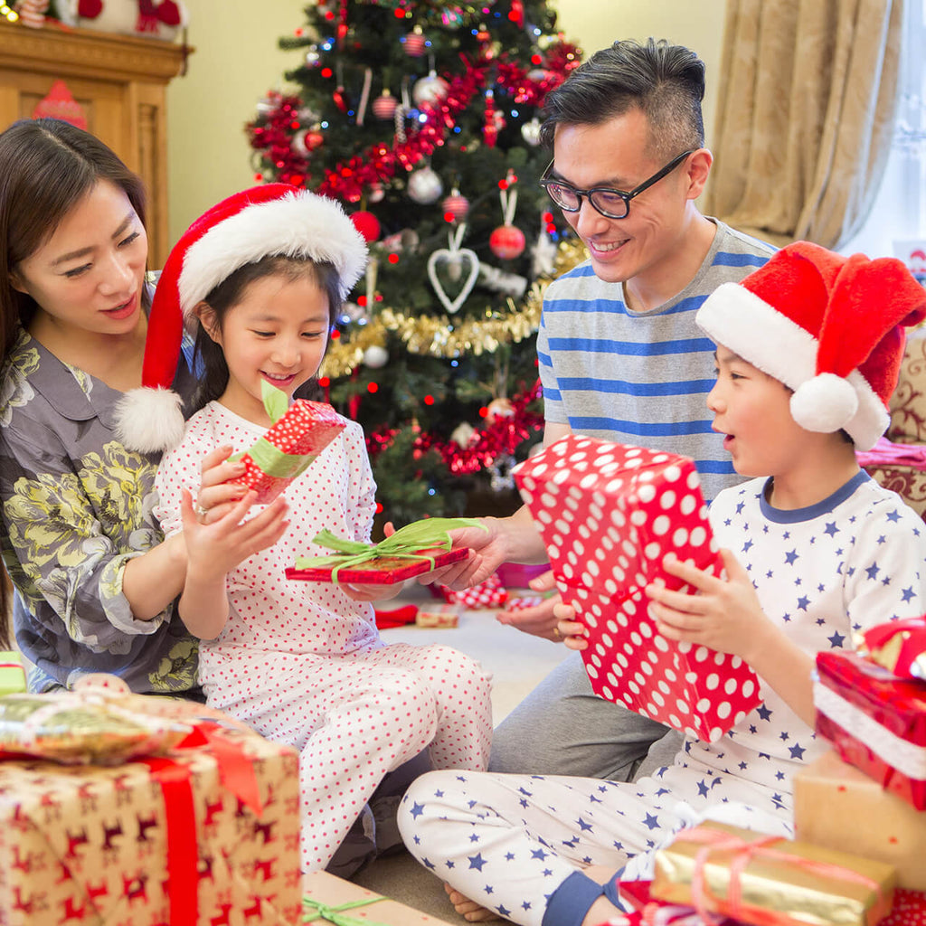 Happy Family Sat In A Circle Opening Christmas Presents By The Tree In Their Pyjamas